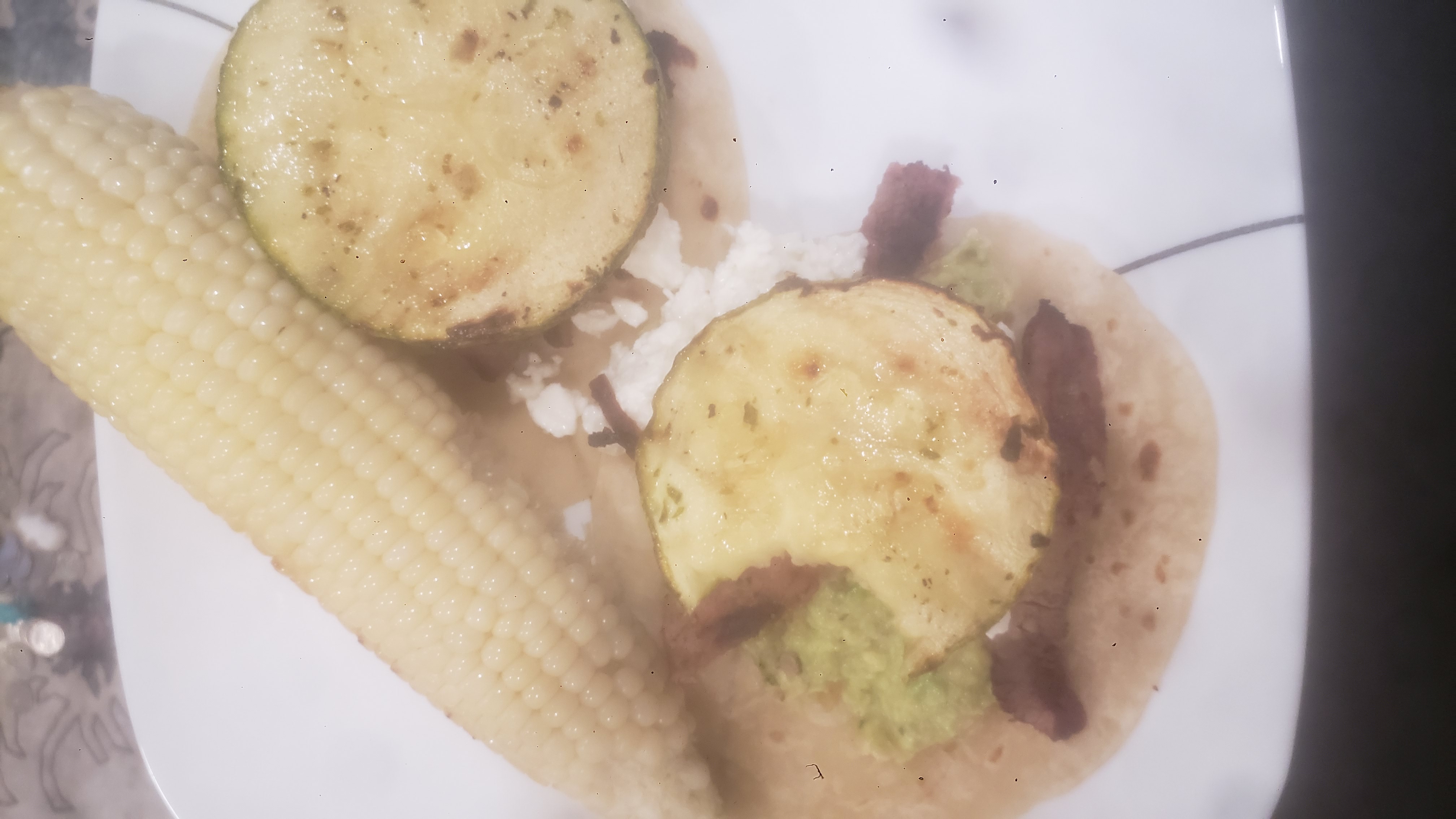 Vegetable filled taco with a grilled corn next to it.